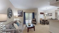This single-floor residence offers a thoughtfully designed layout across several well-defined living spaces. The living room sets a warm tone with neutral-toned carpet, crown molding, and a sliding glass door that allows natural light to fill the room. A dedicated dining area sits adjacent, featuring crown molding, a pendant light fixture, and a window with decorative valance. The kitchen is well-equipped with warm wood cabinetry, ample counter space, a stainless steel range, hardwood-style flooring, and a breakfast bar that provides additional seating and casual dining options. A versatile flex room serves as a home office or sitting area, complete with vaulted ceilings, a sliding glass door, and plush carpeting. The bedroom is generously sized, offering soft carpet, a large sliding glass door with vertical blinds for light control, and ample room for furnishings. Bathrooms include a full bath with a single vanity, wood cabinetry, a tub-shower combination, and tile surround. An additional bathroom area features light tile flooring and a built-in linen cabinet for storage. Throughout the residence, a consistent warm, neutral color palette and carpeted floors create a cohesive and comfortable living environment.