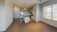 This single-story, one-bedroom, one-bathroom residence features a practical and modern design throughout its generously sized floor plan. The open-concept living and kitchen area serves as the heart of the unit, where rich wood-style flooring, track lighting, and pendant lights over the kitchen island create a warm, functional atmosphere. Large windows and a glass door allow natural light to fill the living space, offering views of the surrounding area.

The kitchen is outfitted with granite countertops, white shaker-style cabinetry, a tile backsplash, a central island with a sink, and a full suite of stainless steel appliances, including a refrigerator, microwave, and electric range. The bedroom features plush carpeting, a ceiling fan, and a window with natural light. It connects to a spacious walk-in closet with built-in shelving and hanging rods for ample storage.

The bathroom includes a granite-topped vanity, wood-style flooring, and a full soaking tub with shower. A dedicated laundry room houses a full-size washer and dryer with additional overhead shelving. Neutral tones and clean finishes throughout give the space a cohesive, move-in-ready appeal.
