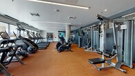 Located at 1420 Oak St in Lakewood, Colorado, this contemporary fitness center offers a comprehensive workout environment designed to support a wide range of exercise routines. The space is laid out across a single floor and features durable rubberized cork flooring throughout, providing both comfort and safety for high-impact activities.

The cardio zone is lined with multiple treadmills positioned along large floor-to-ceiling windows, allowing natural light to fill the area and offering views of the surrounding outdoor environment. Adjacent to this section, a dedicated cycling studio houses several stationary spin bikes alongside a large wall-mounted display screen and built-in cabinetry, creating a functional space for guided workout sessions.

The strength training area is well-appointed with a full array of cable machines, weight benches, free weights, and multi-functional rack systems, all set against a deep charcoal accent wall with integrated shelving for additional equipment storage. Mirrored walls enhance the sense of space and allow for form monitoring during workouts.

A functional training zone rounds out the facility, equipped with punching bags, kettlebells, medicine balls, battle ropes, and resistance tools neatly organized on wall-mounted racks. Architectural details such as linear recessed lighting, structural columns, and a clean neutral color palette give the space a polished, modern aesthetic throughout.