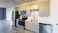 Located in the heart of Miami's vibrant Brickell neighborhood, this modern urban unit at 35 SW 6th Street showcases a sleek, contemporary design with distinctive industrial-inspired elements. Exposed concrete ceilings run throughout the open-plan layout, lending the space a loft-like aesthetic that complements the clean white walls and smooth grey wood-look flooring underfoot.

The open living area is bright and airy, with large floor-to-ceiling windows that frame sweeping city views, flooding the space with natural light. A bold navy blue accent wall adds a touch of color and depth to the living zone.

The kitchen is well-appointed and functional, featuring light wood cabinetry with sleek hardware, stainless steel appliances including a refrigerator, electric range, built-in microwave, and dishwasher, along with a deep stainless steel sink with a professional-style faucet and ample counter space. Track lighting above the kitchen provides focused illumination.

The bedroom area includes a closet with open shelving and rod storage, offering practical organization. The bathroom is finished with large-format neutral stone-look tiles surrounding a soaker tub with chrome fixtures, creating a clean and calming retreat.

The unit also includes an in-unit washer, adding everyday convenience in this well-designed Miami residence.