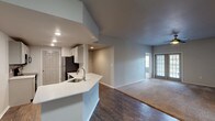 This single-floor residence offers a thoughtfully designed open-concept layout that seamlessly connects the kitchen and living areas. The kitchen is a standout feature, equipped with stainless steel appliances including a refrigerator, microwave, and range, complemented by crisp white cabinetry, quartz countertops, and a peninsula with an integrated sink — ideal for both meal preparation and casual dining. Dark hardwood-style flooring runs throughout the main living and kitchen areas, adding warmth and contrast to the neutral gray walls.

The living area is generously proportioned, with natural light filtering in through windows, creating a bright and welcoming atmosphere. Each bedroom is finished with plush carpeting, ceiling fans with light fixtures, and ample closet space — the primary bedroom notably includes a walk-in closet with built-in shelving. Additional bedrooms feature large windows that invite natural light and offer outdoor views.

The bathrooms are well-appointed; one features a vessel sink atop a quartz vanity with gray cabinetry and a large framed mirror, while the second includes a full tub-shower combination with a quartz vanity. Clean lines, recessed lighting, and a consistent neutral palette throughout give the space a modern, cohesive feel.