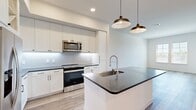 This thoughtfully laid-out one-bedroom, one-bathroom residence offers a clean, modern aesthetic throughout its efficiently organized single floor. The open-concept kitchen and living area serves as the heart of the home, featuring crisp white shaker cabinetry, dark granite countertops, a geometric tile backsplash, and a full suite of stainless steel appliances including a range, over-the-range microwave, and refrigerator. A substantial center island with a built-in sink and pendant lighting above provides additional prep space and casual dining. Light wood-style flooring runs throughout the main living areas, contributing to a bright and airy atmosphere. The living area is bathed in natural light, with access to a private balcony offering outdoor views. The bedroom is comfortably sized, carpeted for warmth, and features dual windows that frame outdoor scenery, along with a ceiling fan. A dedicated closet provides organized storage. The bathroom is finished with large-format tile flooring and includes a glass-enclosed walk-in shower. A hallway connects the private spaces seamlessly, completing this well-appointed and functional residence.