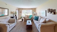This single-story home offers a comfortable and cohesive layout across its living spaces. The living room serves as a central gathering area, finished with plush carpeting, a textured ceiling, and a stone fireplace that adds rustic character. Natural light streams through large windows, and the space comfortably accommodates multiple seating arrangements. The kitchen features warm wood cabinetry, ample counter space, a dual-basin sink, and black appliances including a range, microwave, and refrigerator, all set atop stone-look tile flooring. Two full bathrooms are finished with wood vanities, tile flooring in a mosaic pattern, framed mirrors, and shower-tub combos with decorative curtains. The home includes multiple bedrooms, each carpeted and uniquely styled. One bedroom features a large closet with rich wood bifold doors and a teal color scheme, while another offers a spacious layout with a window view and open shelving. A third bedroom provides a cozy retreat with a wrought-iron bed frame and warm neutral tones. Throughout the home, textured ceilings, warm beige walls, and wood-trimmed doors create a consistent and inviting aesthetic that ties each room together seamlessly.