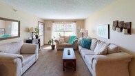 This single-story home offers a comfortable and cohesive layout across its living spaces. The living room serves as a central gathering area, finished with plush carpeting, a textured ceiling, and a stone fireplace that adds rustic character. Natural light streams through large windows, and the space comfortably accommodates multiple seating arrangements. The kitchen features warm wood cabinetry, ample counter space, a dual-basin sink, and black appliances including a range, microwave, and refrigerator, all set atop stone-look tile flooring. Two full bathrooms are finished with wood vanities, tile flooring in a mosaic pattern, framed mirrors, and shower-tub combos with decorative curtains. The home includes multiple bedrooms, each carpeted and uniquely styled. One bedroom features a large closet with rich wood bifold doors and a teal color scheme, while another offers a spacious layout with a window view and open shelving. A third bedroom provides a cozy retreat with a wrought-iron bed frame and warm neutral tones. Throughout the home, textured ceilings, warm beige walls, and wood-trimmed doors create a consistent and inviting aesthetic that ties each room together seamlessly.