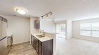 Located in Beavercreek, Ohio, this two-bedroom, two-bathroom residence offers a well-organized single-floor layout with a thoughtful mix of finishes and functional design. The kitchen is a standout feature, equipped with stainless steel appliances including a refrigerator, range, microwave, and dishwasher, complemented by dark espresso cabinetry, light quartz countertops, and wood-look plank flooring. A peninsula with a double-basin sink opens directly to the living room, which is brightened by a ceiling fan and glass patio doors leading to a private balcony with outdoor views. Track lighting over the kitchen peninsula adds a modern touch. The carpeted living area provides a comfortable transition to the rest of the home. The primary bedroom is generously sized with a large window allowing natural light and direct access to a private en-suite bathroom, which features wood-look tile flooring, a vanity with dark cabinetry, and a walk-in closet. The second bedroom also features plush carpet and a spacious closet with built-in shelving. The second bathroom includes a tiled shower-tub combination and matching finishes. Carpeted stairs lead to additional access points within the building. The overall aesthetic is clean and neutral throughout.
