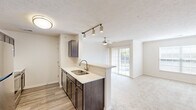 Located in Beavercreek, Ohio, this two-bedroom, two-bathroom residence offers a well-organized single-floor layout with a thoughtful mix of finishes and functional design. The kitchen is a standout feature, equipped with stainless steel appliances including a refrigerator, range, microwave, and dishwasher, complemented by dark espresso cabinetry, light quartz countertops, and wood-look plank flooring. A peninsula with a double-basin sink opens directly to the living room, which is brightened by a ceiling fan and glass patio doors leading to a private balcony with outdoor views. Track lighting over the kitchen peninsula adds a modern touch. The carpeted living area provides a comfortable transition to the rest of the home. The primary bedroom is generously sized with a large window allowing natural light and direct access to a private en-suite bathroom, which features wood-look tile flooring, a vanity with dark cabinetry, and a walk-in closet. The second bedroom also features plush carpet and a spacious closet with built-in shelving. The second bathroom includes a tiled shower-tub combination and matching finishes. Carpeted stairs lead to additional access points within the building. The overall aesthetic is clean and neutral throughout.