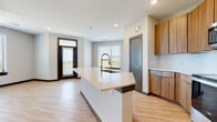 This single-floor residence showcases a clean, contemporary design with light hardwood-style flooring flowing throughout the main living areas. The open-concept kitchen serves as the heart of the home, anchored by a generous center island with a quartz countertop and an undermount sink. Warm wood cabinetry lines the walls, complemented by a full suite of stainless steel appliances, including a refrigerator, range, and built-in microwave. The kitchen opens seamlessly into the living area, creating an airy, connected feel enhanced by recessed lighting and natural light from multiple windows with blinds. The spacious main bedroom features plush carpeting, a ceiling fan, and a window with an outdoor view of greenery. The primary bathroom is well-appointed with an extended wood vanity, quartz countertop, and direct access to a walk-in closet. A second bathroom mirrors the modern aesthetic with a matching wood vanity and clean finishes. A dedicated in-unit laundry space accommodates a full-size washer and dryer with built-in shelving for added storage. Throughout the residence, a neutral color palette, dark baseboards, and consistent modern fixtures create a cohesive and polished ambiance.
