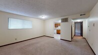 Located at 58 Gahl Terr in Reading, Ohio, this single-floor unit offers a straightforward, functional layout across several connected rooms. The spacious living area is finished with wall-to-wall carpeting and neutral cream-toned walls, complemented by dark baseboards that provide a clean visual contrast. A window fitted with horizontal blinds allows natural light to filter into the space, and a ceiling-mounted light fixture provides additional illumination. The living area opens directly into the kitchen, making the overall flow practical and accessible.

The kitchen is equipped with warm-toned oak cabinetry that extends along the upper and lower walls, offering generous storage. White appliances include an electric range, over-the-range microwave, dishwasher, and a full-size refrigerator. Light-toned vinyl tile flooring and a single-basin sink with a window above complete the kitchen's functional design.

The bedroom areas feature the same neutral carpeting and cream walls, each receiving natural light through blinds-covered windows. One bedroom includes access to a walk-in closet area visible through an open doorway. The bathroom is fitted with tile flooring, a wood-toned vanity with a white countertop, and a full-size tub and shower combination with a grab bar and chrome fixtures.