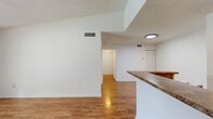 Located in Miami Gardens, FL, this single-floor, two-bedroom, one-bathroom residence offers a well-organized layout across a comfortable footprint. The open-concept living room is a standout feature, showcasing warm hardwood-style flooring that reflects natural light streaming in through large sliding glass doors. Those doors lead to a private balcony with an outdoor railing, offering pleasant views of surrounding greenery. The adjacent kitchen is efficiently designed with a pass-through peninsula topped with granite-style countertops, dark wood cabinetry, and stainless steel appliances, all set on clean tile flooring. Both bedrooms feature soft wall-to-wall carpeting and bright white walls. The primary bedroom includes a closet with louvered bifold doors and access to the hallway. The second bedroom is equally well-lit, with a large window framing outdoor views. The full bathroom is finished with neutral tile surrounds in the tub/shower combination, complemented by a granite-top vanity and tile flooring. A hallway connects all rooms, with a dedicated closet for additional storage. Textured ceilings throughout add a classic touch to this straightforward and functional Miami Gardens home.