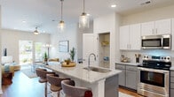 Located in Surf City, NC, this well-appointed one-bedroom, one-bathroom residence offers a thoughtfully designed open-concept layout with a coastal-inspired aesthetic. The kitchen and living area form the heart of the home, anchored by a large granite-topped island with seating, pendant lighting in brushed gold fixtures, and stainless steel appliances. Two-tone cabinetry — white upper and grey lower — pairs with a classic subway tile backsplash for a clean, modern look. A walk-in pantry provides generous additional storage. Warm hardwood-style flooring flows throughout the main living areas, extending into the bright and open living room, which features recessed lighting, a ceiling fan, and glass doors that open onto a private balcony with natural light and outdoor views. The generously sized bedroom offers a ceiling fan, natural light through a large window, and direct access to a spacious walk-in closet outfitted with wire shelving and dual hanging rods. The bathroom is finished with a glass-enclosed combination tub and shower. Throughout, the neutral palette and airy finishes create a relaxed, coastal atmosphere that reflects the spirit of its Surf City location.