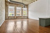 This generously sized two-bedroom, one-bathroom loft in Birmingham, Alabama, blends industrial character with modern updates across a single expansive floor. Rich hardwood floors run throughout the space, complementing the exposed brick walls that lend a raw, historic authenticity to the interior. Soaring ceilings with visible structural beams and exposed ductwork reinforce the industrial aesthetic, creating a dramatic sense of vertical space.

The open-plan kitchen and living area serves as the heart of the unit. The kitchen is outfitted with sage-green cabinetry, granite countertops, stainless steel appliances including a refrigerator and dishwasher, and a central island — ideal for both cooking and entertaining. A long corridor with whitewashed brick walls and polished hardwood floors connects the living spaces to the private rooms.

Both bedrooms feature tall ceilings, ceiling fans, and hardwood floors. The primary bedroom offers generous proportions with ample room for large furnishings. Large windows in the bedrooms frame views of the surrounding downtown Birmingham streetscape, flooding the rooms with natural light. The bathroom includes a double-sink granite vanity, tiled flooring, and a shower-tub combination. Additional amenities include a laundry room, utility room, and two closets, rounding out this distinctive urban residence.