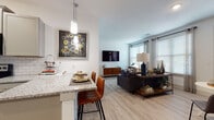 This well-designed single-floor residence offers a thoughtful layout that balances open communal spaces with private retreats. The open-concept living and dining area is anchored by large windows that invite abundant natural light, complemented by light wood-look flooring and a bold charcoal accent wall that adds depth and character. The living room provides generous space for relaxing and entertaining, with multiple windows offering pleasant outdoor views.

The kitchen is a standout feature, showcasing gray shaker-style cabinetry, gleaming granite countertops, a classic white subway tile backsplash, and a full suite of stainless steel appliances. A peninsula with seating serves as both a functional workspace and a casual dining spot, seamlessly connecting the kitchen to the living area.

A well-proportioned hallway with light wood flooring leads to the two bedrooms. The primary bedroom features a ceiling fan, plush carpeting, and a dramatic navy accent wall, while the second bedroom is bright and airy with large windows and neutral tones. Each bedroom offers comfortable proportions and ample natural light.

Both bathrooms are finished with granite vanity tops and gray cabinetry. One bathroom includes a tub/shower combination, while the other features a glass-enclosed walk-in shower. The overall aesthetic throughout is clean, modern, and cohesive.