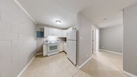 This efficiently designed single-floor unit offers a practical layout comprising a living room, kitchen, bedroom, full bathroom, and closet. Light beige tile flooring runs consistently throughout the space, creating a clean, unified aesthetic.

The kitchen features white shaker-style cabinetry with granite-look countertops, a white electric range, and a full-size white refrigerator. A cinder block accent wall adds a distinctive architectural character, and a built-in electrical panel is housed within the kitchen area. Flush-mount ceiling lighting provides bright, even illumination.

The living area is open and straightforward, with neutral gray walls, white baseboards, and a wall-mounted PTAC heating and cooling unit. A window with blinds allows natural light to filter into the space, and a paneled entry door provides direct access.

The bedroom is a cozy, private space featuring a cinder block exterior wall with a window fitted with blinds, contributing to solid insulation and a quiet atmosphere. Neutral tones keep the room feeling clean and adaptable.

The full bathroom is finished in white, featuring a combination tub and shower unit, a white vanity with storage, and tile flooring that matches the rest of the unit. The clean, simple design ensures functionality throughout.

Overall, the unit presents a consistent, no-frills aesthetic with durable finishes suitable for everyday living.