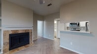 This single-floor residence is thoughtfully designed with a cohesive neutral color palette and quality finishes throughout. The main living area makes an immediate impression with its distinctive herringbone-patterned hardwood-style flooring, which extends seamlessly across the open-concept space. A standout feature of the living room is the tile-surround fireplace with a classic white mantel, flanked by built-in shelving that adds both function and character. A ceiling fan overhead and a large window fitted with horizontal blinds allow natural light to fill the room comfortably.

The kitchen is designed for efficiency, featuring a galley-style layout with ample white cabinetry above and below, light countertops, a double-basin sink, and a full suite of stainless steel appliances including a refrigerator, range, and over-the-range microwave. A pass-through counter connects the kitchen to the living area, enhancing the open feel of the shared space.

The bedroom continues the warm, neutral aesthetic with plush carpeting, a generously sized window with outdoor views, and a ceiling-mounted light fixture. Throughout the residence, consistent details such as white baseboards, soft taupe walls, and vinyl plank flooring in the kitchen create a unified, well-maintained interior environment.