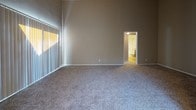 This single-floor residence offers a well-designed layout that balances comfort and functionality throughout its living spaces. The open-concept living and dining area immediately draws the eye upward with striking vaulted ceilings that lend an airy, expansive feel to the space. Warm neutral tones on the walls complement the plush carpeting underfoot, while large windows with vertical blinds allow natural light to filter in generously.

The galley-style kitchen is efficiently arranged with rich dark espresso cabinetry, light countertops, and durable hardwood-style flooring. Ample upper and lower cabinet storage lines both sides of the kitchen, which is equipped with a full suite of appliances including a stove and refrigerator. A window at the end of the kitchen brings in additional natural light.

The bedroom is generously proportioned, featuring soaring vaulted ceilings and soft carpeting. A sliding glass door opens directly onto a private balcony, offering outdoor space and abundant natural light. The bedroom also provides direct access to the full bathroom.

The bathroom is clean and functional, featuring hardwood-style flooring, a dark wood vanity with a light countertop, a large mirror, and a full soaking tub and shower combination. Overhead lighting completes the well-appointed space. Throughout the residence, the consistent use of dark wood accents and neutral tones creates a cohesive and inviting aesthetic.