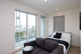 Located in the heart of West Los Angeles, Unit 401 at 1775 Beloit Ave offers a thoughtfully designed co-living space spread across two floors. The unit showcases a clean, modern aesthetic with light wood flooring, recessed lighting, and a neutral color palette throughout.

The main living area features a well-appointed kitchenette integrated into a seamless wall of taupe cabinetry, complete with a microwave, sink, and ample storage. A built-in desk with overhead cabinetry and a wall-mounted TV provide both functionality and style, while a comfortable sofa and bed make this a true live-work environment.

Private rooms are efficiently designed, each featuring Murphy beds that fold away to maximize floor space, paired with sleek sofas and large windows that invite natural light and offer views of the surrounding neighborhood. Light wood flooring and recessed lighting maintain a bright, airy feel in each room.

The bathrooms are finished to a high standard, featuring large-format grey tile surrounds, soaking tub and shower combinations with sliding glass enclosures, and floating vanities with undermount sinks and warm taupe cabinetry. One bathroom includes a bidet-equipped toilet, adding a modern touch.

Overall, this co-living unit delivers a contemporary, functional, and well-finished living environment in a prime Los Angeles location.