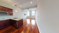 Located at 1401 N 5th St in Philadelphia's vibrant Northern Liberties neighborhood, this single-floor residence combines modern finishes with thoughtful design throughout. Rich, warm-toned hardwood flooring flows seamlessly across the entire unit, anchoring each space with a polished, cohesive aesthetic.

The open-concept living and dining area is bathed in natural light from large, industrial-style grid windows that frame sweeping city views. Crown molding and a ceiling fan add both elegance and practicality to the generous living space.

The gourmet kitchen is a standout feature, appointed with deep mahogany cabinetry, striking granite countertops, and a full suite of stainless steel appliances including a gas range, refrigerator with ice maker, built-in microwave, and dishwasher. A large kitchen island with pendant lighting provides additional prep space and casual seating.

A well-appointed hallway with built-in storage leads to the bedroom, which offers ample natural light through corner windows with open city views and continues the rich hardwood flooring. The bathroom is elegantly finished with large-format gray-toned tile, a jetted soaking tub, and a glass sliding shower enclosure, creating a refined, spa-like atmosphere. A smart home panel near the entrance adds a modern technological touch to this meticulously designed residence.