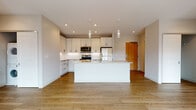 Located on the vibrant Larchmere Boulevard in Cleveland, Ohio, this modern single-floor unit offers a thoughtfully designed layout with contemporary finishes throughout. The open-concept kitchen serves as the centerpiece of the living area, showcasing crisp white shaker cabinetry with black hardware, a white subway tile backsplash, light stone countertops, and a generous central island with pendant lighting overhead. Stainless steel appliances, including a range, over-the-range microwave, and refrigerator, complete the well-appointed kitchen. Warm hardwood flooring extends throughout the main living area, creating a bright and cohesive atmosphere. The bedrooms are carpeted for comfort and feature large windows that allow abundant natural light and views of the surrounding neighborhood. A ceiling fan adds functionality to each bedroom. The primary bedroom connects to a spacious walk-in closet with built-in shelving and leads directly to a private en-suite bathroom. The bathrooms are finished with light blue-gray shaker vanities, granite-style countertops, large mirrors, dark tile flooring, and matte black hardware accents. A walk-in shower is featured in the primary bath, while a second full bathroom provides additional convenience.