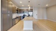 This well-appointed single-floor unit offers a thoughtfully designed open-concept layout with consistent light wood-style flooring throughout. The kitchen serves as the heart of the home, showcasing taupe shaker-style cabinetry, a classic white subway tile backsplash, and granite countertops. A large center island with pendant lighting provides generous prep space and casual seating. Stainless steel appliances, including a French door refrigerator, electric range, built-in microwave, and dishwasher, complete the kitchen's modern appeal.

The spacious living area extends naturally from the kitchen, featuring a ceiling fan and a window that invites natural light. Multiple bedrooms offer a calm, neutral palette with light taupe walls, light wood flooring, ceiling fan fixtures, and windows fitted with blinds that frame outdoor views. 

Two bathrooms mirror the home's design language with granite-topped vanities and taupe cabinetry. One bathroom features a tiled soaking tub with grab bars, while the other offers a glass-enclosed walk-in shower. Both include large mirrors and brushed nickel fixtures. A dedicated laundry area houses a full-size washer and dryer, adding everyday convenience to this clean, contemporary space.