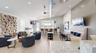 Authentix McHenry's single-story amenity center is designed with a clean, contemporary aesthetic that prioritizes both function and comfort. The welcoming entry features a granite-topped reception desk, pendant lighting, shiplap accent walls, and a branded entry mat, setting the tone for the well-appointed spaces beyond.

The open-concept clubhouse lounge is a highlight of the facility, boasting soaring ceilings with exposed industrial ductwork, a large ceiling fan, and recessed lighting. A retractable garage-style window wall floods the space with natural light and frames outdoor views, while light wood-look flooring ties the area together. The lounge offers multiple distinct seating zones, including curved upholstered sofas, a banquette dining area with a wall-mounted TV, bar-height seating along the kitchen counter, and a cozy conversation nook adorned with a sculptural wooden wall piece. A kitchenette with stainless steel appliances and granite countertops serves the space with ease.

The fitness center is equally impressive, outfitted with a comprehensive suite of Matrix cardio equipment — including treadmills, ellipticals, and a stair climber — alongside cable strength machines. Whitewashed exposed brick walls feature an inspirational Muhammad Ali quote, adding personality and motivation to every workout session.