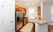 This single-floor residence at 400 Riverfront Blvd in Elmwood Park, New Jersey, presents a clean, well-maintained interior with a functional and cohesive design throughout. The main living area is spacious and filled with natural light from multiple windows dressed with horizontal blinds. Polished hardwood flooring runs across the open living space, reflecting light and lending warmth to the neutral, cream-toned walls trimmed with crisp white baseboards.

The kitchen is well-appointed, featuring warm-toned wood cabinetry, granite countertops with a subtle mosaic tile backsplash, and a full suite of stainless steel appliances including a refrigerator with ice and water dispenser, gas range, and microwave. Track lighting overhead and a window at the end of the galley-style layout keep the space bright and practical.

The bedroom offers plush carpeting, a window with natural light, and a calm, neutral palette. Two bathrooms serve the unit — one featuring a glass-enclosed walk-in shower, mosaic tile flooring, and a dark wood vanity, while the second offers a similarly styled vanity with light tile flooring. A hallway connects the rooms efficiently, with additional door access providing storage flexibility throughout the unit.