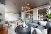 Located in the heart of Midtown Atlanta, this elegantly designed single-floor space offers a seamlessly flowing open layout that balances comfort, functionality, and refined aesthetics. Striking herringbone-patterned hardwood flooring runs throughout the main areas, creating a warm yet sophisticated foundation that contrasts beautifully with the dramatic dark-painted ceilings overhead.

The space is divided into several distinct yet interconnected zones. A generous lounge area anchors the layout, furnished with plush sectional seating, a bold round dark coffee table, and an eclectic patterned accent chair beneath a sculptural brass chandelier. Floor-to-ceiling windows flood the space with abundant natural light and frame sweeping views of the surrounding Atlanta skyline and treetops.

A dedicated entertainment zone features a large wall-mounted display screen alongside a textured wall panel treatment and additional seating. Nearby, a foosball table and casual seating area with woven chairs add a playful, social dimension to the space.

Built-in cabinetry with glass accents and mirrored panels lines a central corridor, providing an elegant transitional passage between zones. A counter bar with cushioned stools offers a flexible spot for gathering or working. Toward the back, a private area with carpet flooring and subtle lighting offers a quieter retreat. Throughout, curated greenery, layered lighting, and thoughtful furnishings create a polished, welcoming ambiance.