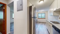 This 2-bedroom, 1-bathroom unit is efficiently laid out across a single floor, offering a functional and comfortable living environment. The galley-style kitchen is a standout feature, equipped with white shaker cabinetry, granite-look countertops, a stainless steel refrigerator, and a stainless steel range, all complemented by hardwood-style vinyl plank flooring that extends through the main living areas. The kitchen also includes a sink with a modern faucet and ample upper and lower cabinet storage. Connecting hallways provide a logical flow between rooms. The spacious primary bedroom features dual windows with blinds that invite natural light and outdoor views, hardwood-style flooring, and a wall-mounted air conditioning unit alongside baseboard heating. The second bedroom is finished with neutral-toned carpet, a window with blinds, and baseboard heating, creating a cozy and quiet retreat. The bathroom is clean and straightforward, featuring white tile walls, a tub and shower combination with a curtain, and tile flooring. Textured ceilings are present throughout the unit, contributing to a classic residential aesthetic. An electrical panel is conveniently accessible within the unit.