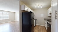 This single-floor residential unit offers a practical and well-appointed layout designed for comfortable everyday living. Warm wood-look flooring runs consistently throughout the space, creating a cohesive and inviting atmosphere accented by neutral, greige-toned walls and crisp white trim.

The kitchen is efficiently designed and equipped with black appliances, including a full-size refrigerator and electric range. White shaker-style cabinetry provides ample storage above and below the counters, while granite-patterned countertops and a stainless steel double-basin sink add a polished finish. A track light fixture overhead ensures bright, functional illumination. A textured ceiling is present throughout the unit, adding a classic touch.

The open living area is spacious and versatile, featuring a ceiling fan with light, wood-look flooring, and wall vents for climate control. Large windows fitted with horizontal blinds allow natural light to fill the room, contributing to an airy feel.

The bedroom is generously proportioned with its own window offering natural light, and a closeted door provides additional utility. The bathroom is clean and functional, featuring a white vanity with a granite-patterned countertop, a full-size soaking tub, and wood-look flooring that ties the space together with the rest of the unit.