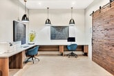Located at 1901 East 1st Street in Santa Ana, California, this contemporary office space offers a well-designed, single-room layout that maximizes functionality within a compact footprint. The interior features polished concrete floors throughout, lending an industrial yet refined aesthetic that ties the space together cohesively.

The primary work area is anchored by a long, built-in workstation with a light wood and gray composite surface, comfortably accommodating multiple workstations. Sleek blue ergonomic task chairs complement the modern design. The workstation is illuminated by a pair of matte black pendant lights with brass accents, suspended from a clean white ceiling fitted with recessed lighting and integrated HVAC vents. Abstract line artwork displayed above the desk adds a curated, professional touch.

A standout architectural feature is the large sliding barn door crafted from richly textured reclaimed wood, mounted on an exposed black steel track — providing both a functional partition and a bold visual focal point.

A dedicated lounge or breakout area features built-in booth seating upholstered in vibrant teal, paired with warm wood-toned tables. A colorful geometric mural in soft yellows, blues, and grays enlivens the wall behind the seating, creating an inviting, energetic atmosphere. A framed artwork and recessed lighting complete this zone. The space also includes a built-in area accommodating office equipment such as a printer, rounding out its practical amenities.