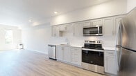 Located in the desirable NW 25th corridor of Portland, Oregon, this single-floor unit showcases a clean, contemporary design with light-toned luxury vinyl plank flooring running throughout the entire space, creating a cohesive and modern aesthetic.

The kitchen is a standout feature, equipped with a full suite of stainless steel appliances including a refrigerator, electric range, over-the-range microwave, and dishwasher. Gray shaker-style cabinetry with brushed nickel hardware lines the walls, complemented by white quartz countertops and a single-basin undermount sink. The open layout allows the kitchen to flow naturally into the main living area, which is illuminated by recessed lighting and benefits from an open, airy feel.

The bedroom receives generous natural light through multiple windows offering views of surrounding greenery, enhancing the bright, welcoming atmosphere. The bathroom features an extended vanity with white cabinetry, a quartz countertop, and direct access to a walk-in closet with built-in shelving. A dedicated in-unit laundry area with a washer provides added convenience. The overall design is clean, minimal, and move-in ready.