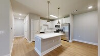Located at 3795 Bismarck Ct in Oxford, Florida, this single-story residence presents a clean, contemporary design throughout its well-appointed interior. The kitchen serves as a central highlight, showcasing crisp white shaker-style cabinetry extending to the ceiling, a classic white subway tile backsplash, and a full suite of stainless steel appliances including a French door refrigerator, electric range, built-in microwave, and dishwasher. A generously sized center island with a bright white countertop anchors the space, illuminated by a pair of brushed brass pendant lights that add a warm, refined accent. Light wood-tone flooring runs throughout the kitchen and connecting areas, enhancing the airy, modern aesthetic. The bedrooms feature neutral-toned carpet, ceiling fans for comfort, and windows that allow natural light to filter in. Closet access is conveniently integrated into the bedroom layout. The bathroom is finished with a wide-format vanity featuring a white countertop and brushed nickel hardware, a large mirror, and a soaking tub enclosed by floor-to-ceiling white subway tile. Neutral gray walls and clean white trim are consistent throughout, contributing to a cohesive, move-in-ready atmosphere.