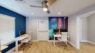Located at 1001 Pinemont Drive in Houston, Texas, this single-floor business center serves as a functional and stylish amenity space for Dominion at Oak Forest Apartments. The workspace is designed with productivity in mind, featuring multiple individual workstations outfitted with modern white adjustable desks and ergonomic rolling chairs, accommodating several users simultaneously.

The interior is finished with warm wood-look flooring throughout, providing a clean and contemporary aesthetic. Bold blue accent walls energize the space, complemented by crisp white trim and neutral gray walls. A striking full-wall graphic mural depicting the iconic Houston Heights sign serves as a vibrant focal point, reinforcing the local identity of the community.

Recessed lighting and ceiling fans ensure the space remains well-lit and comfortable. A large window with white horizontal blinds allows natural light to filter in, brightening the main work area. An expansive bank of tall, shaker-style white cabinetry provides generous built-in storage, keeping the workspace organized and uncluttered.

The space also includes a dedicated printer and office equipment station, enhancing its utility for everyday business tasks. An open doorway connects the business center to an adjacent lounge area, offering a comfortable retreat just steps away. Overall, the space delivers a professional yet welcoming environment for residents to work and study.