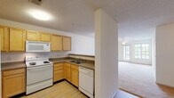 Located at 2792 Stantonsburg Rd in Greenville, NC, this single-floor unit offers a practical and comfortable layout designed for everyday living. The kitchen is outfitted with light wood cabinetry, a double-basin sink, a white electric range, a built-in microwave, and a dishwasher, all set on easy-care hardwood-style flooring. A half-wall peninsula separates the kitchen from the adjoining living area, creating an open, connected feel while maintaining a distinct sense of each space. The living area is generously sized, featuring soft wall-to-wall carpeting, a ceiling fan with light fixture, and a set of French doors that flood the room with natural light and provide access to the outdoors. Additional bedrooms are carpeted and well-lit, each benefiting from windows that bring in natural light, ceiling fans, and ample closet space including a paneled double-door closet in one room. The bathrooms feature hardwood-style flooring, a tub-shower combination, toilet, and a vanity with warm wood cabinetry and a large mirror. Throughout the unit, textured ceilings, neutral wall tones, and clean finishes contribute to a bright and move-in-ready atmosphere.