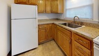 This three-floor unit is designed with functionality and comfort in mind. The main living level greets you with warm, honey-toned hardwood flooring that extends throughout, complemented by neutral cream-toned walls that create a bright and clean atmosphere. A staircase with a classic white banister connects the floors, while a sliding closet door provides convenient storage. The open layout flows directly into the kitchen, which is equipped with oak cabinetry, granite-style countertops, a stainless steel sink, and white appliances, all set atop tile flooring with a window that brings in natural light.

The upper level hosts multiple well-proportioned rooms, each featuring the same hardwood flooring and baseboard heating. Windows fitted with blinds allow for natural light and outdoor views. One room includes a wall-unit air conditioner for added climate control. The bathroom features a full-size soaking tub with a shower, white subway tile surround, a window for ventilation, and tile flooring.

The lower level offers a spacious open basement area with a concrete floor, painted walls, overhead lighting, and a metal staircase leading to the floors above, making it well-suited for storage or utility use.