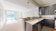 This two-story home offers a thoughtfully designed layout spread across two evenly sized floors. The main level features an open-concept kitchen and living room, where dark espresso cabinetry pairs with granite countertops and pendant lighting above a breakfast bar peninsula. The kitchen transitions seamlessly into the carpeted living area, which benefits from a sliding glass door that fills the space with natural light and provides outdoor access. Hardwood-style flooring in the kitchen adds a clean contrast to the soft carpet of the living room. A hallway, closet, and one of the three bathrooms round out the main floor. The attached garage offers additional utility with a standard roll-up door.

Upstairs, the primary bedroom is a generously sized retreat with vaulted ceilings, multiple windows, and its own walk-in closet with built-in shelving. A second well-lit bedroom also enjoys natural light from large windows. Both upstairs bedrooms are finished with plush carpet and neutral wall tones. The upper level is served by two additional bathrooms, including one featuring a walk-in glass-enclosed shower with built-in niches. Throughout the home, a consistent neutral palette and clean architectural lines create a bright, functional, and welcoming atmosphere.