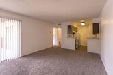This single-floor unit offers a straightforward, functional layout with a clean, neutral aesthetic throughout. The main living area is generously proportioned, featuring wall-to-wall carpet in a warm tan tone, crisp white walls, and a textured popcorn ceiling. A large sliding glass door dressed with vertical blinds fills the space with natural light and provides outdoor views, creating an open and airy atmosphere.

Additional rooms mirror this design approach, each equipped with ceiling fans, sliding glass doors with vertical blinds, and the same carpeted flooring, ensuring consistency throughout the unit. The natural light flowing through the sliding doors offers pleasant outdoor views of surrounding greenery.

The bathroom features a wide, speckled light-toned countertop with an integrated sink, set atop dark espresso-stained cabinetry. A large wall-spanning mirror enhances the sense of space, and a towel bar provides practical functionality.

The kitchen, visible in the overview scan, is fitted with white appliances including a range, complemented by dark cabinetry that echoes the bathroom's design. The entry door, finished with gold-tone hardware, adds a subtle traditional detail. Overall, the space maintains a clean, move-in ready presentation with a cohesive, understated design.