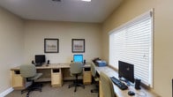 This single-floor business center is designed to provide a functional and comfortable workspace for those needing access to computing resources. The room features multiple workstations arranged along two walls, each equipped with desktop computers, keyboards, and mice, allowing several users to work simultaneously without feeling cramped.

The workstations are built into light wood cabinetry with granite-style countertops, offering a polished and cohesive aesthetic. Each station includes under-counter storage, keeping the workspace tidy and organized. A printer is conveniently accessible, positioned centrally for shared use among workstation users.

The walls are painted in a warm neutral tone, contributing to a calm and focused atmosphere. Two framed landscape artworks add a decorative touch, softening the utilitarian nature of the space. A large window fitted with white horizontal blinds allows natural light to filter in while maintaining privacy and reducing glare on screens.

Carpeted flooring adds a quiet, comfortable underfoot feel, and recessed overhead lighting ensures the space remains well-lit regardless of the time of day. Overall, the business center is thoughtfully arranged to balance practicality with a welcoming, professional ambiance.