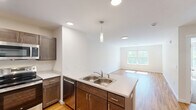 Located at 375 Autumn Pond Way in Essex Junction, Vermont, this well-appointed one-bedroom, one-bathroom residence offers a thoughtfully designed single-floor layout with a clean, modern aesthetic. The open-concept kitchen and living area serves as the heart of the home, featuring warm hardwood flooring, recessed lighting, and a central peninsula with a double-basin sink and pendant light overhead. The kitchen is outfitted with rich, dark-toned cabinetry, stainless steel appliances including a refrigerator, range, and built-in microwave, and crisp white countertops that provide a striking contrast. The spacious living area flows naturally from the kitchen, offering an open canvas bathed in natural light. The private bedroom is generously sized, finished with plush carpeting, and includes a window that frames leafy outdoor views, lending a peaceful, natural ambiance. A dedicated closet adds practical storage. The bathroom is clean and functional, featuring a full tub/shower combination, and conveniently houses a stacked in-unit washer and dryer — a practical amenity. Throughout the residence, neutral walls, white trim, and consistent finishes create a bright, cohesive atmosphere well suited to comfortable everyday living.
