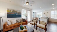 This single-floor residence is designed with a clean, contemporary aesthetic, combining functionality with modern finishes. The open-concept living area is anchored by wood-look flooring, a ceiling fan with integrated lighting, and generous natural light streaming through multiple windows fitted with plantation-style blinds. The living space flows seamlessly into a dedicated dining area, which benefits from a wall of windows offering outdoor views, creating a bright and airy atmosphere throughout.

The kitchen is well-equipped, featuring gray shaker-style cabinetry, granite-look countertops, stainless steel appliances, and a central island with a built-in sink — an efficient and stylish workspace that connects directly to the living and dining zones.

A carpeted primary bedroom features a bold teal accent wall, ceiling-height details, and direct access to a private en-suite area. A second bedroom offers plush carpet, a ceiling fan, natural light, and ample space. The bathroom includes a granite-topped vanity with gray cabinetry, wood-look flooring, and a shower-tub combination. A clean hallway with panel doors connects the private rooms, maintaining an organized and cohesive layout throughout.