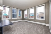 This single-floor urban residence offers a thoughtfully designed layout with a clean, modern aesthetic throughout. The open-concept kitchen serves as a functional centerpiece, featuring warm wood cabinetry extending to the ceiling, dark countertops, stainless steel appliances including a range, microwave, and refrigerator, and a substantial kitchen island with an integrated sink topped by a pendant light. The kitchen flows naturally into the living area, where light-toned flooring transitions into plush carpeting.

The main living area is generously proportioned and bathed in natural light, thanks to an impressive array of large double-hung windows that frame views of the surrounding urban cityscape. These windows are a defining feature of the space, bringing the energy of the city indoors while filling the room with daylight.

The bedrooms continue the carpeted aesthetic and maintain a bright, neutral palette with crisp white walls. A light wood sliding door and a connecting hallway with light hardwood flooring add warmth and cohesion between rooms. One of the standout storage features is a dedicated walk-in closet fitted with wire shelving systems along multiple walls, providing ample organization space. The overall ambiance is modern and urban, well-suited for comfortable city living.