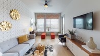 This single-floor residence at 3825 N 25th St in Tacoma, Washington, offers a thoughtfully designed open-concept layout with modern finishes and a cohesive contemporary aesthetic. Light-toned hardwood flooring flows throughout the space, creating visual continuity between the living, dining, and kitchen areas.

The living room is a standout feature, showcasing a bold geometric accent wall, large windows that invite abundant natural light and outdoor views, and a ceiling fan. The space is generously proportioned, lending an airy, comfortable atmosphere suited for both relaxing and entertaining.

The kitchen is well-appointed with tall white upper cabinetry, warm wood-toned lower cabinets, quartz countertops, and a full suite of stainless steel appliances including a side-by-side refrigerator, electric range, and built-in microwave. A peninsula with an undermount sink provides additional prep space and seating. Adjacent to the kitchen, a built-in shelving nook offers practical storage and display options.

The bathroom continues the modern design language with a wide-format vanity featuring rich wood cabinetry, a white quartz countertop, an oversized mirror, and light-wood flooring. The overall ambiance of the space is clean, bright, and polished, reflecting a contemporary urban sensibility throughout.