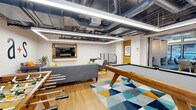 This single-floor commercial space in Berkeley, CA (94704) combines a professional work environment with thoughtfully designed recreational areas. The space features an industrial-modern aesthetic throughout, characterized by exposed ductwork and structural elements set against a clean white ceiling, complemented by warm wood flooring and contemporary linear lighting.

The central game lounge serves as a social hub, anchored by a solid wood pool table with a cue rack built into the wall. A wall-mounted flat-screen TV, gray sectional seating, and a vibrant geometric area rug in blue, teal, and gold tones create an inviting lounge atmosphere. Adjacent to the lounge, a dedicated work zone provides individual alcove-style workstations with built-in desks, adjustable chairs, and warm accent lighting, offering focused work settings separated from communal areas.

A casual dining or meeting area features built-in wood banquette seating, white tables, orange accent chairs, and a decorative hexagonal moss wall installation beneath a muted blue ceiling. A branded reception or lounge area near the entrance displays the "a+s" logo prominently, with gray sofas and a bold yellow-and-gray patterned rug establishing a welcoming first impression.
