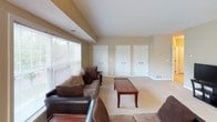 This single-floor space offers a thoughtfully organized layout with distinct functional areas flowing naturally from one to the next. The living room serves as the central gathering space, featuring neutral beige walls, soft carpet flooring, and a large picture window with horizontal blinds that fills the room with natural light and offers views of surrounding greenery. Vaulted ceiling detailing adds architectural interest, while three white paneled closet doors along one wall provide generous built-in storage.

The kitchen is well-equipped and functional, featuring white cabinetry that extends to the ceiling for maximum storage, a central island topped with a striking dark granite counter, and light hardwood-style flooring. White appliances including a refrigerator, range, built-in microwave, and dishwasher are neatly integrated throughout, complemented by a double sink beneath a window.

The bathroom includes both a standalone glass-enclosed shower and a tiled soaking tub, with tile flooring and warm neutral walls creating a clean, practical environment. The dedicated laundry room houses a full-size washer and dryer beneath white upper cabinetry, providing additional storage and utility convenience. The bedroom, visible in the floor plan, completes this well-rounded layout.