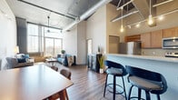 Located on Cuming Street in Omaha, NE, this 2-bedroom, 2-bathroom loft delivers a striking industrial-chic aesthetic with soaring ceilings, exposed metal ductwork, and concrete structural elements throughout. The open-concept living, dining, and kitchen area forms the heart of the space, bathed in natural light from floor-to-ceiling windows that frame outdoor views of the surrounding cityscape. Rich hardwood-style flooring flows continuously underfoot, anchoring the warm, urban character of the interior.

The kitchen features warm wood cabinetry, stainless steel appliances, and a peninsula with bar seating — ideal for casual dining. A dedicated dining area is defined by a dramatic original exposed brick wall, adding raw texture and historic character to the space. The living room benefits from expansive windows, creating a bright and airy retreat.

The spacious primary bedroom offers generous proportions, floor-to-ceiling windows, and a closet, while the second bedroom continues the loft's cohesive industrial style with exposed structural details. Both bathrooms are finished with wood-toned cabinetry, stone-look countertops, and glass-enclosed showers with hardwood-style flooring. A hallway connects the private quarters, completing this well-designed urban residence.