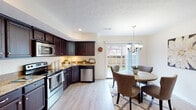 This two-story home at 7600 Ashton Park Cir in Louisville, Kentucky offers a well-designed layout across two floors. The kitchen is a standout feature, showcasing rich dark cabinetry, granite-look countertops, and a full suite of stainless steel appliances including a refrigerator, range, microwave, and dishwasher, all set atop light wood-style flooring. Under-cabinet lighting adds a warm, functional touch to the workspace.

Adjacent to the kitchen, the dining area is bright and inviting, with a sliding glass door that opens to an outdoor view, flooding the space with natural light. An elegant chandelier overhead completes the setting. The living room is generously sized, featuring a ceiling fan, large windows with sheer drapery, and light flooring that creates an airy, welcoming atmosphere.

Upstairs, the bedroom offers a comfortable retreat with plush carpeting and convenient access to a full bathroom. The bathrooms are clean and well-appointed, with one featuring a tub-shower combination and another offering a single vanity with white cabinetry and a large mirror. Light wood-style flooring carries throughout the main living areas, unifying the home's design with a consistent, modern aesthetic.