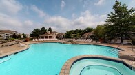 Located at 5412 Edwards Farms Rd in Columbus, Ohio, this single-level community amenity space is centered around a standout resort-style outdoor pool area. The expansive swimming pool features a freeform design with clear, inviting blue water, complemented by a separate spa with decorative stone accents along its border. Surrounding the pool is a generous sundeck outfitted with rows of lounge chairs, providing ample space for relaxation and recreation. A covered pavilion or clubhouse structure is visible in the background, offering a shaded gathering area for residents. The entire space is framed by mature trees that provide natural privacy and a lush, park-like ambiance. The community's residential buildings can be seen in the backdrop, reinforcing the sense of an integrated, well-appointed neighborhood environment. The grounds are well-maintained and enclosed by perimeter fencing, ensuring a safe and comfortable outdoor experience. Overall, this amenity space is designed to foster community and leisure, offering residents a polished outdoor retreat with a welcoming atmosphere under open skies in the heart of Columbus.