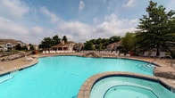Located at 5412 Edwards Farms Rd in Columbus, Ohio, this single-level community amenity space is centered around a standout resort-style outdoor pool area. The expansive swimming pool features a freeform design with clear, inviting blue water, complemented by a separate spa with decorative stone accents along its border. Surrounding the pool is a generous sundeck outfitted with rows of lounge chairs, providing ample space for relaxation and recreation. A covered pavilion or clubhouse structure is visible in the background, offering a shaded gathering area for residents. The entire space is framed by mature trees that provide natural privacy and a lush, park-like ambiance. The community's residential buildings can be seen in the backdrop, reinforcing the sense of an integrated, well-appointed neighborhood environment. The grounds are well-maintained and enclosed by perimeter fencing, ensuring a safe and comfortable outdoor experience. Overall, this amenity space is designed to foster community and leisure, offering residents a polished outdoor retreat with a welcoming atmosphere under open skies in the heart of Columbus.
