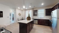 This single-story home offers a thoughtfully designed open-concept layout that seamlessly connects the kitchen, dining, and living areas. The kitchen is a standout feature, showcasing rich dark-espresso cabinetry, white quartz countertops, a classic subway tile backsplash, and stainless steel appliances including a dishwasher and range. A central island with pendant lighting provides additional prep space and a natural gathering point. Light-toned luxury vinyl plank flooring runs throughout the main living areas, enhancing the bright, airy feel.

The dining area sits adjacent to the kitchen and benefits from a glass door that invites natural light. The living room features the same warm flooring and offers a comfortable, open atmosphere. A dedicated office or flex room is carpeted and features a large window overlooking the exterior, making it an ideal workspace or secondary bedroom.

The bedroom is generously sized, with plush carpet, a ceiling fan, and a large window. It connects to a spacious walk-in closet with dual hanging rods and ample shelving. The full bathroom is finished with matching dark cabinetry, white countertops, wood-look flooring, and a full tub-shower combination. A dedicated in-unit laundry area with a full-size washer and dryer completes this functional and stylish home.