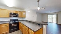 Located at 1000 Old Brook Road in Charlottesville, VA, this multi-level home offers four bedrooms and two bathrooms across a well-utilized floor plan. The open-concept kitchen and living area forms the heart of the home, featuring warm honey-toned cabinetry, dark granite-style countertops, and a peninsula breakfast bar with pendant lighting overhead. Black appliances, including a refrigerator, range, and built-in microwave, complement the kitchen's functional design, while wood-style flooring runs throughout the main living areas. A stacked washer and dryer unit is conveniently tucked within the kitchen space. The living room benefits from a sliding glass door that invites natural light and provides outdoor access. A carpeted staircase with a dark handrail connects the levels of the home. The bedrooms are finished with soft wall-to-wall carpeting and feature windows that bring in natural light. The primary bedroom includes a sliding-door closet with built-in shelving. Both bathrooms are equipped with wood-toned vanities, mirrored storage, and vinyl plank flooring. The overall aesthetic is clean and neutral, offering a versatile canvas well-suited to a variety of living arrangements.