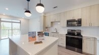 This contemporary apartment in Durham, NC, showcases a thoughtfully designed living space with a focus on modern aesthetics and functionality. The heart of the home is a stylish kitchen featuring light-toned cabinetry, quartz countertops, and stainless steel appliances, including a side-by-side refrigerator and built-in microwave. A large central island provides additional workspace and casual seating.

The open floor plan seamlessly connects the kitchen to the living areas, creating a spacious feel. Globe pendant lights add a touch of elegance to the overall design. The bathroom boasts a clean, minimalist look with a glass-enclosed shower, modern fixtures, and ample vanity space. 

Bedrooms are carpeted for comfort, while the main living areas feature durable wood-look flooring. Large windows allow natural light to flood the space, and a ceiling fan in the bedroom offers additional comfort. The apartment's neutral color palette provides a blank canvas for personal decor styles.

Storage is plentiful throughout, with numerous cabinets in the kitchen and built-in closets in other areas. This well-appointed apartment combines style and practicality, perfect for modern urban living.